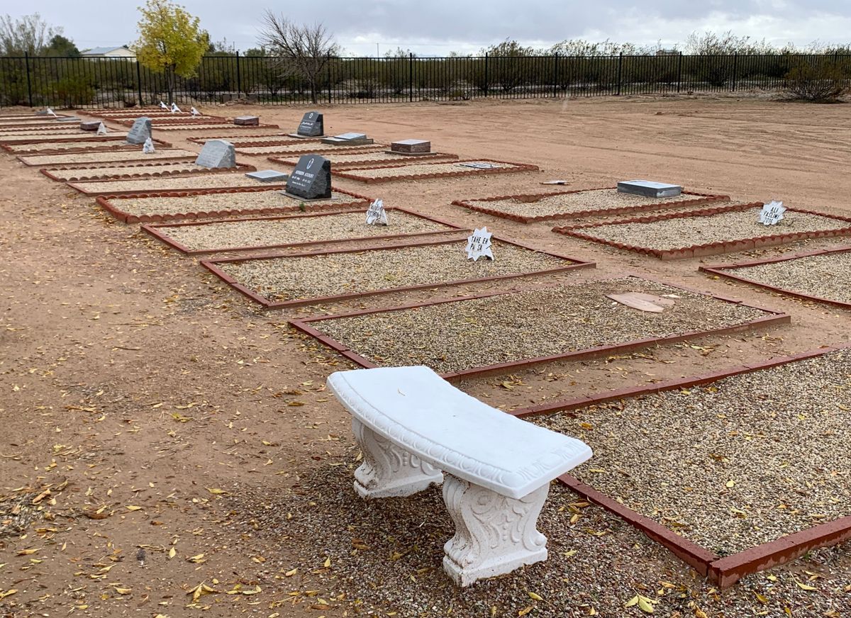 A row of gravesites in the sand, each lined in brick and covered with small desert stones.